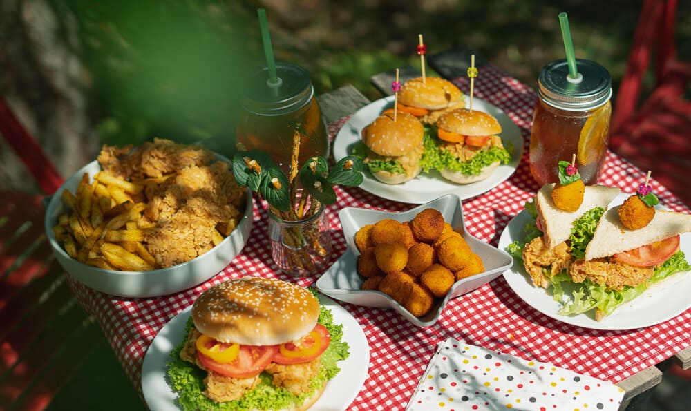 una mesa llena de comida deliciosa como pollo frito, hamburguesas, bolitas de patatas y sándwiches