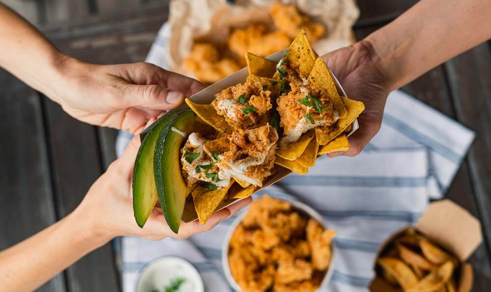 tiras de pollo crujiente una bandejita con nachos, tiras de pollo y trozos de aguacate en las manos
