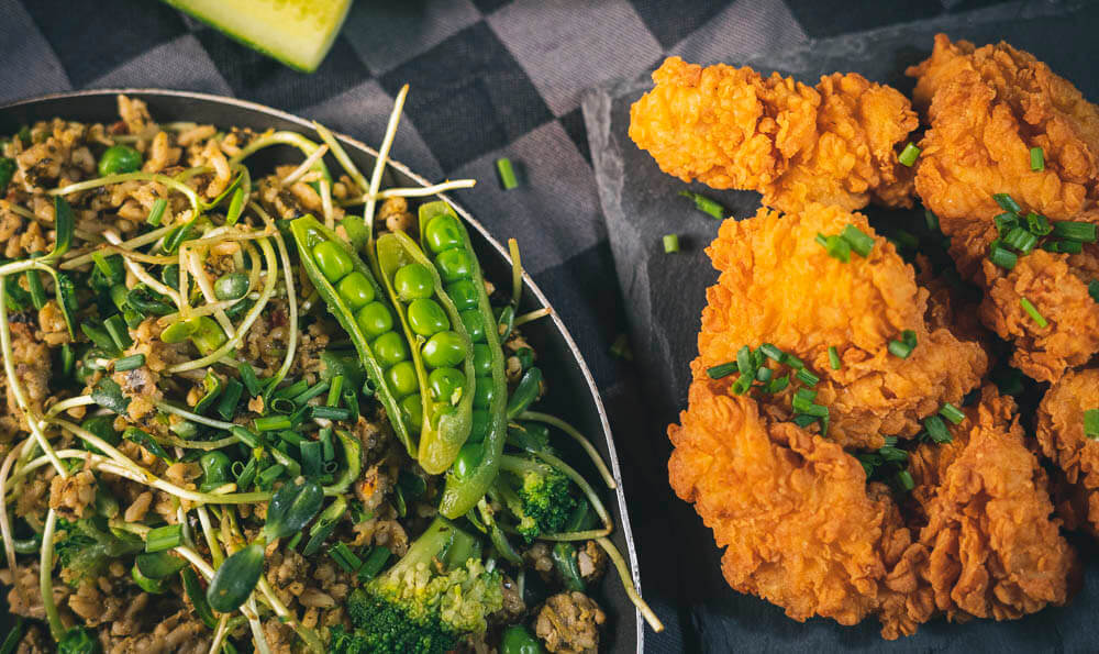 un plato de arroz, verduras y pollo rebozado