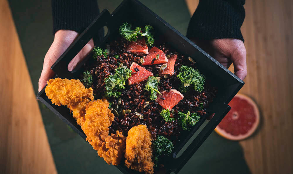 un plato lleno de arroz salvaje, pomelo, pollo rebozado y col rizada